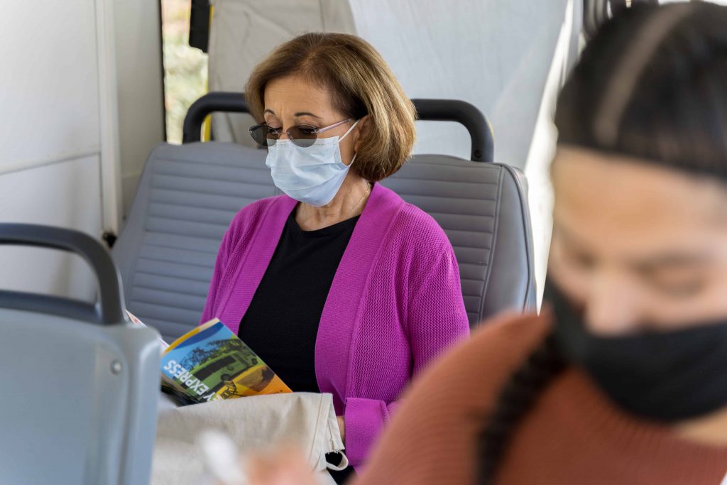 Mujer en suéter morado con máscara leyendo Valley Express libro de autobuses