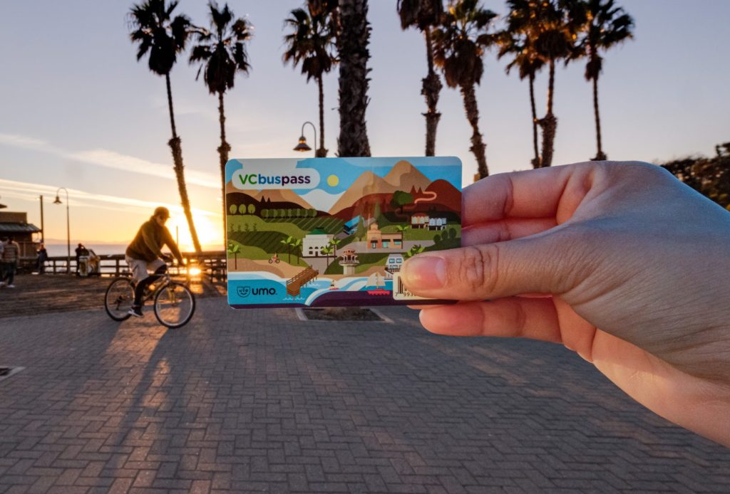 Hand holding VCBussPass with sunset and cyclist in background