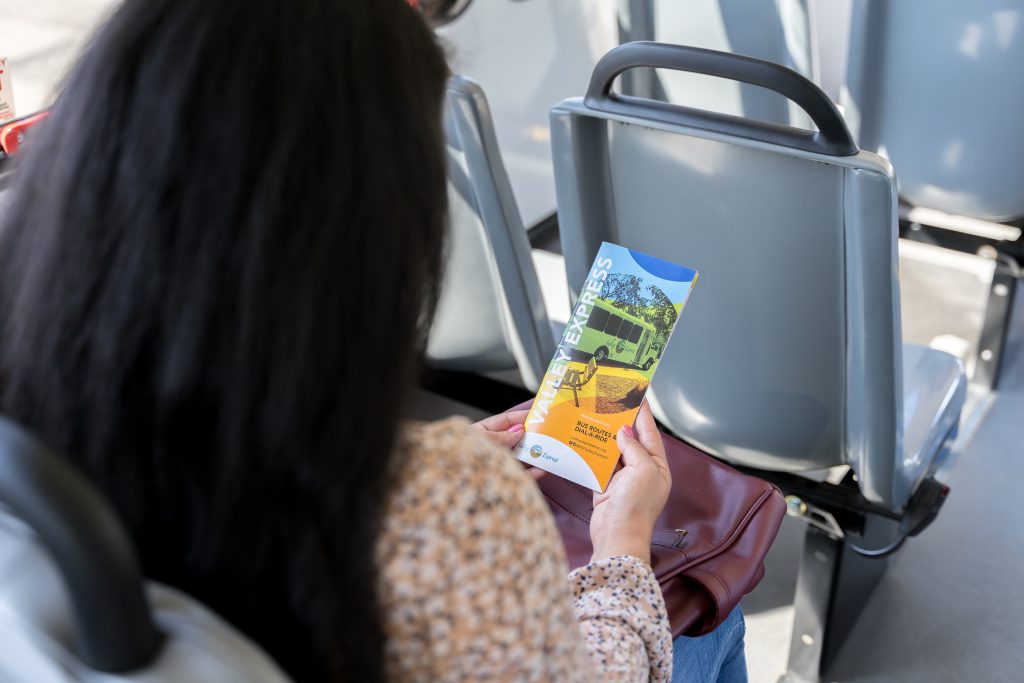 Mujer en suéter morado con máscara leyendo Valley Express libro de autobuses